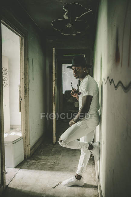 Стильный мужчина, прислонившийся к стене в заброшенном коридоре — стоковое фото