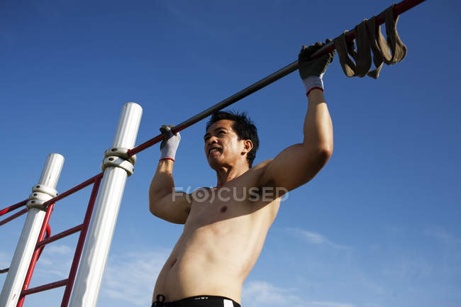 BARCELONA, SPAIN - 10 July, 2011: Shirtless man doing chin-ups on background of blue sky. — Stock Photo