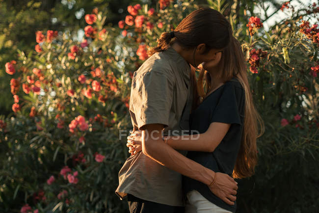 Vista lateral de abraçar casal beijando sobre plantas florescendo no pano de fundo — Fotografia de Stock