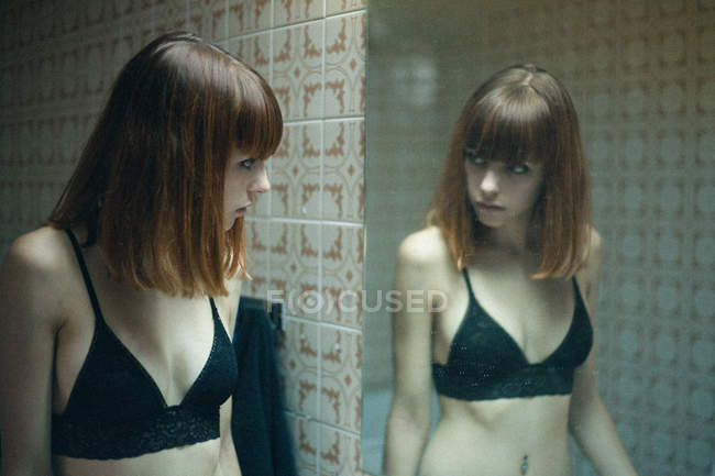 Руда дівчина в чорному бюстгальтері дивиться на дзеркало — стокове фото