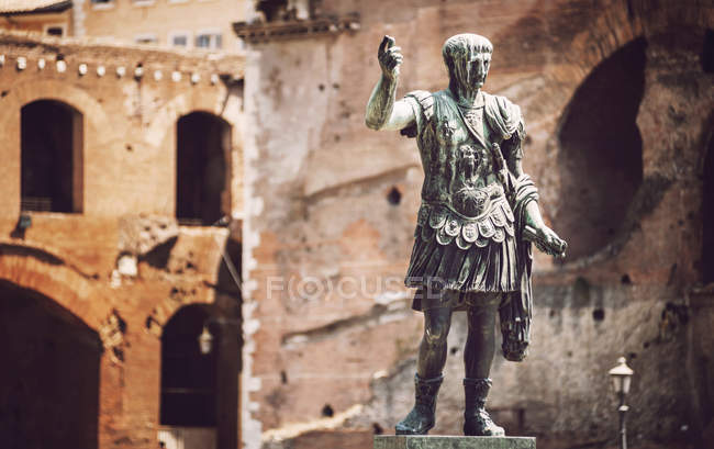 Statue of roman emperor Trajan over antique facades — Stock Photo