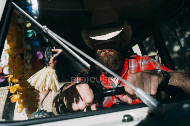 Portrait of anonymous bearded man sitting at drivers seat behind wind screen and holding steering wheel — Stock Photo
