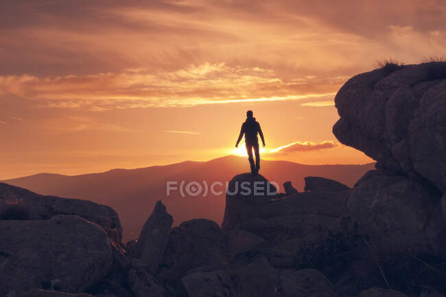 Silueta de hombre en la cumbre en una espectacular puesta de sol enmarcada por rocas - foto de stock