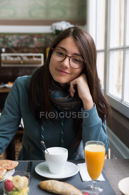 Porträt einer lächelnden brünetten Frau, die sich beim Frühstück im Café an die Hand lehnt — Stockfoto