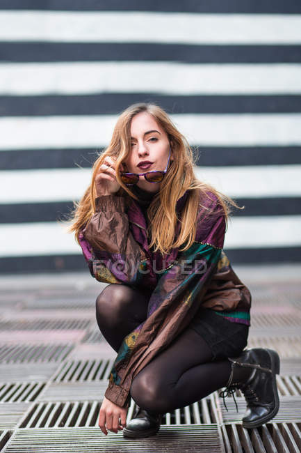 Giovane ragazza alla moda seduta in tozzo e guardando la fotocamera . — Foto stock