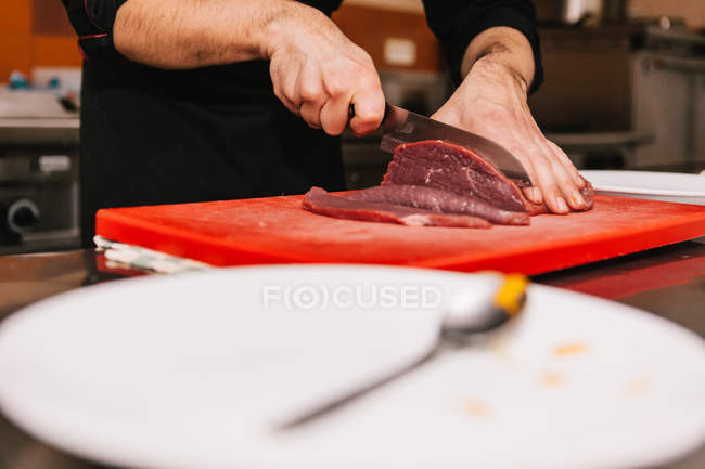 Vue de niveau de surface des mains masculines tranchant la viande à bord au restaurant cuisine — Photo de stock