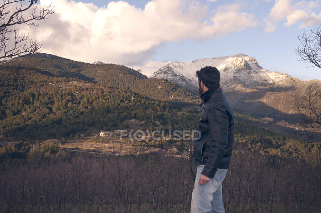 Uomo con giacca di pelle nel bosco una fredda giornata primaverile con montagne innevate sullo sfondo — Foto stock