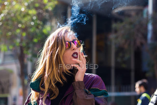Menina usando lábios escuros fumando na rua . — Fotografia de Stock