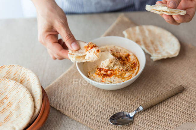 Mani immergendo il pane pita nell'hummus — Foto stock
