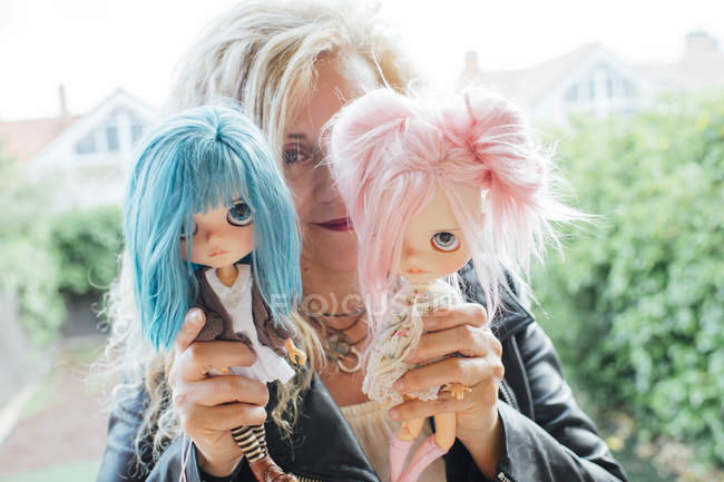 Porträt einer blonden reifen Frau, die zwei Puppen vor der Kamera zeigt — Stockfoto