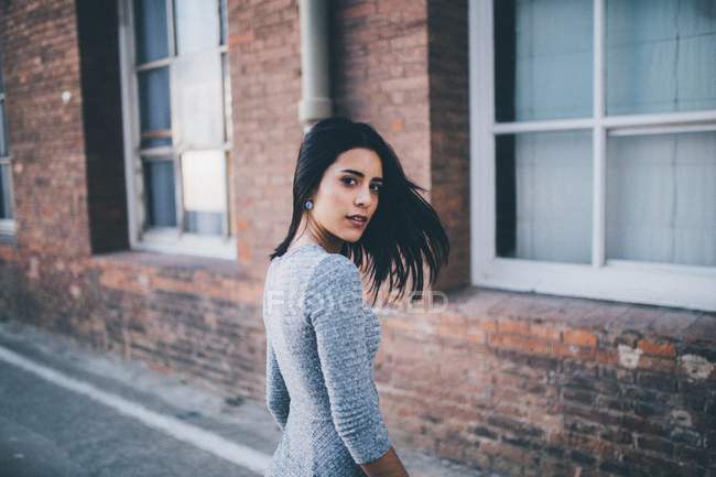 Brunette girl looking over shoulder at camera over brick facade on background — Stock Photo