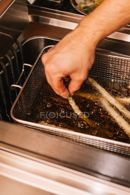 Visão de perto da mão masculina colocando espargos no óleo de fritura — Fotografia de Stock