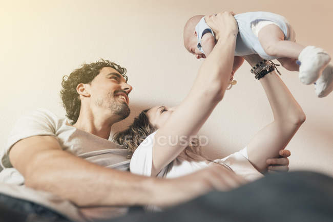 Счастливая молодая пара держит новорожденного ребенка в воздухе — стоковое фото