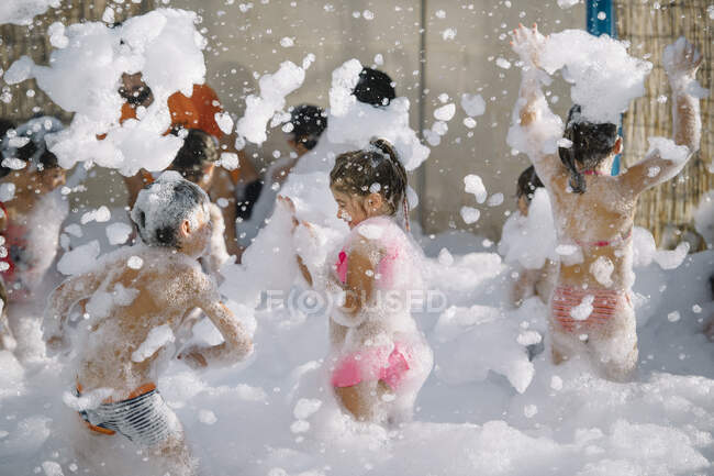 Gruppo di bambini che si divertono in schiuma bianca giocando tutti insieme in cortile. — Foto stock