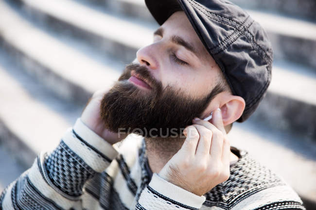 Portrait of bearded man with eyes closed putting earphones to  ears. — Stock Photo