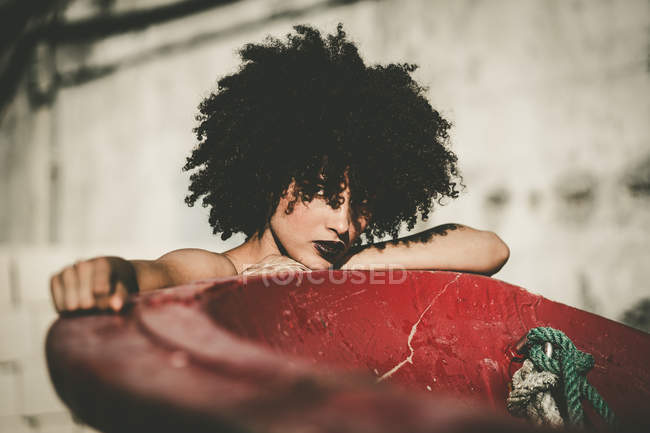Chica con el pelo rizado se apoya en la construcción roja y seductora mirando a la cámara - foto de stock