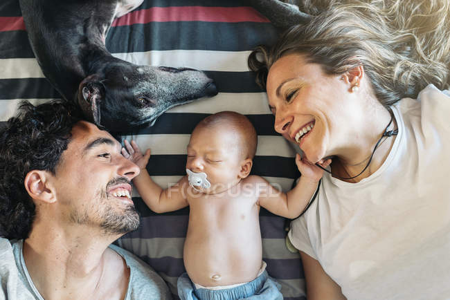 Счастливая молодая пара с новорожденным ребенком и собакой, лежащей на кровати — стоковое фото