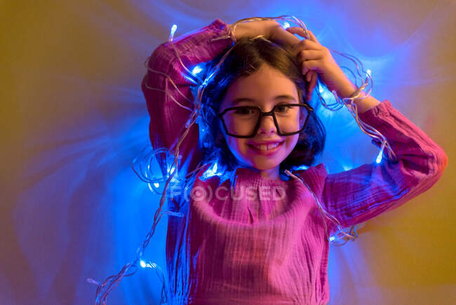 Primo piano di una bambina con occhiali falsi che gioca con le luci di Natale — Foto stock