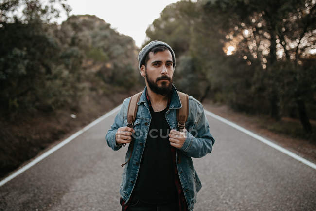 Homme avec sac à dos debout sur la route et regardant de côté — Photo de stock