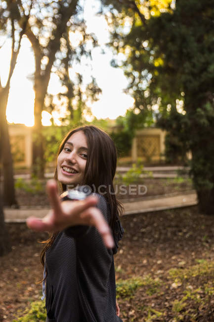 Souriant jeune femme tirant la main à la caméra pendant au parc . — Photo de stock