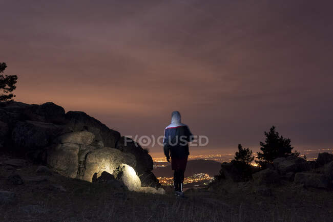 Uomo sulla cima di una montagna e godendo di vista sul cielo notturno e le luci della città — Foto stock