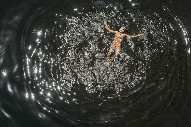 Вид сверху на молодую женщину в оранжевом бикини, купающуюся в воде при солнечном свете — стоковое фото