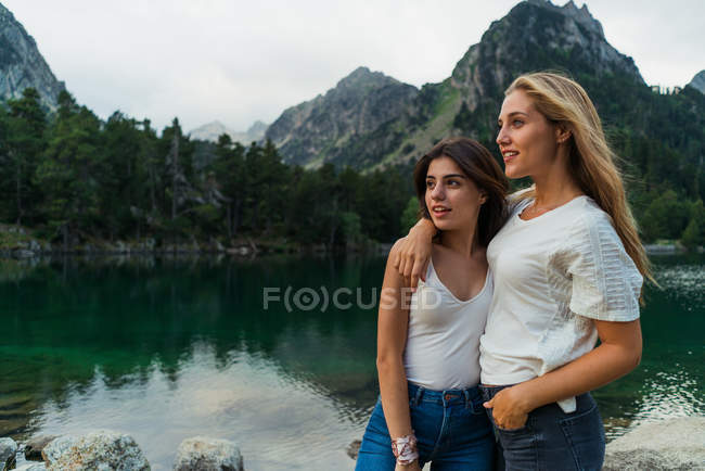 Abrazando chicas posando en el lago en las montañas - foto de stock