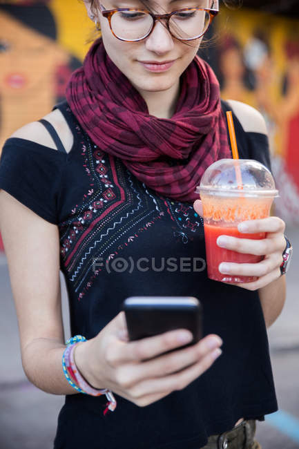 Hübsche junge Frau surft beim Smoothie auf dem Smartphone — Stockfoto
