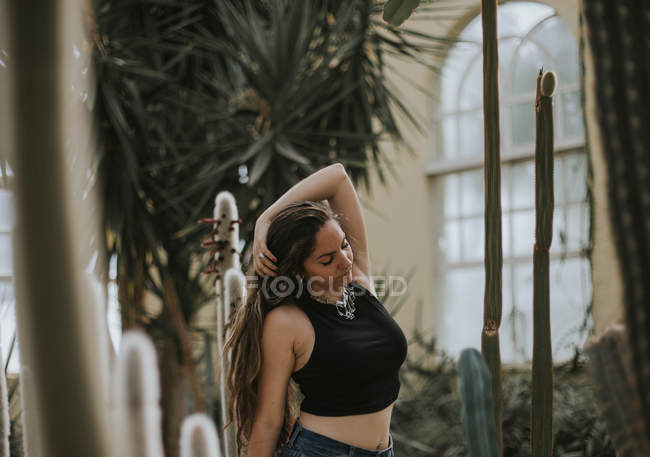 Portrait of brunette girl posing at botanical garden and touching hair — Stock Photo