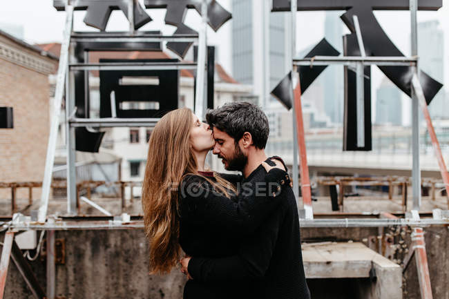 Side view of girl kissing boyfriend 's forehead on rooftop — стоковое фото