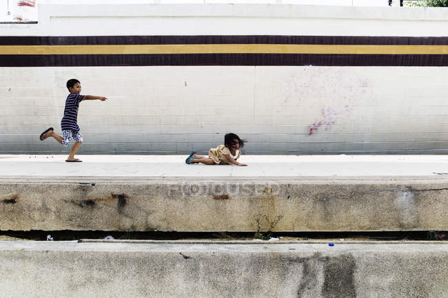 KAULA LUMPUR, MALASIA - 18 DE ABRIL DE 2016: Niño pequeño riendo y señalando a una chica tendida en el suelo - foto de stock