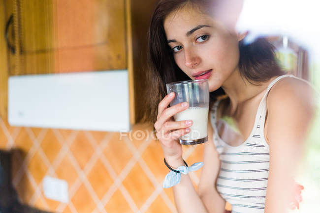Mujer bonita bebiendo vaso de leche en la cocina - foto de stock