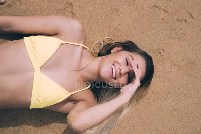 Усміхнена модель лежить на піску і дивиться на камеру — стокове фото