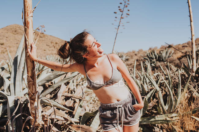 Funny girl with tongue out and eyes closed posing by cacti — Stock Photo