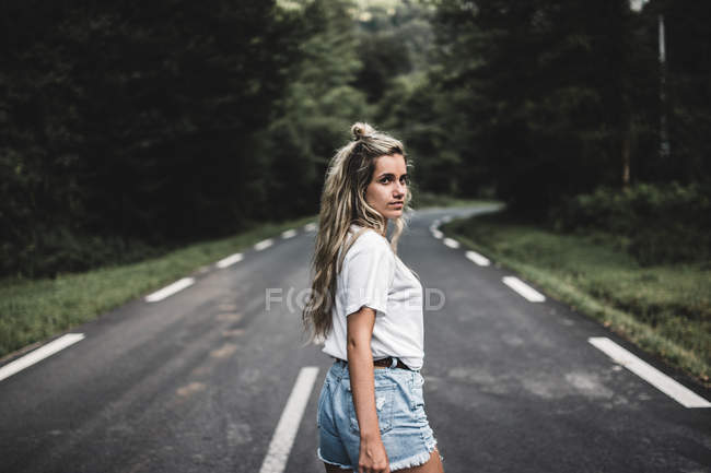 Mulher bonita andando na estrada na floresta e olhando sobre o ombro — Fotografia de Stock