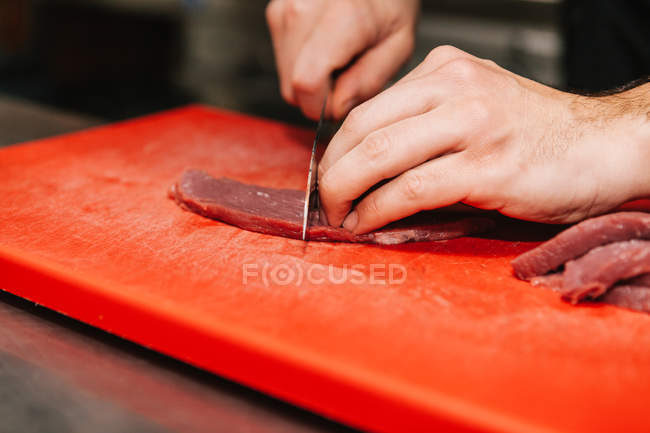 Close-up vista de mãos masculinas cortando carne em placa de plástico vermelho — Fotografia de Stock