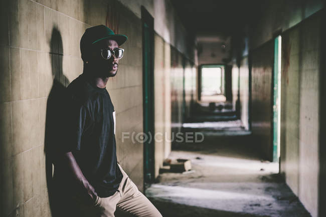 Stylish  man leaning on wall on long hallway in wrecked  building. — Stock Photo