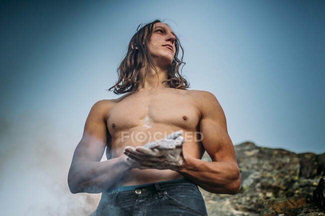 Bottom view of athletic climber with long wavy hair, talcing his arms. — Stock Photo