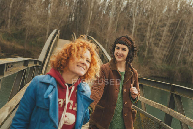 Young women walking on a bridge holding hands. Horizontal outdoors shot. — Stock Photo