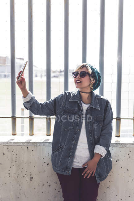 Cheerful young woman taking selfie in the street in sunny day. Vertical outdoors shot. — Stock Photo