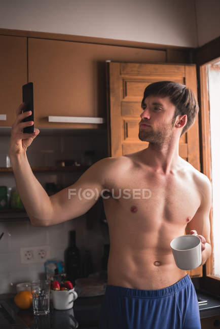 Man with white cup hand posing for selfie in kitchen — Stock Photo