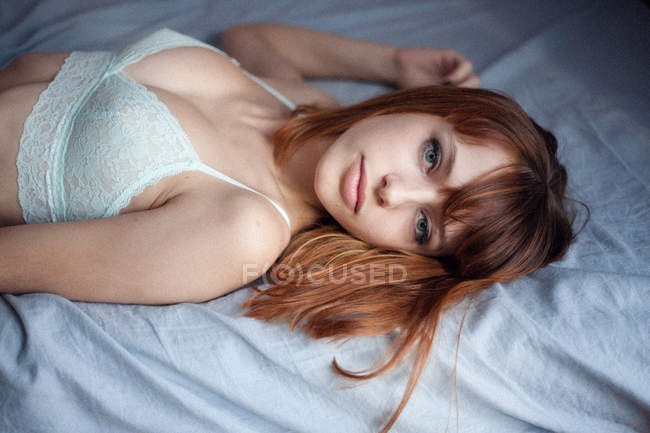 Chica pelirroja sensual en ropa interior de encaje acostado en la cama y mirando a la cámara - foto de stock