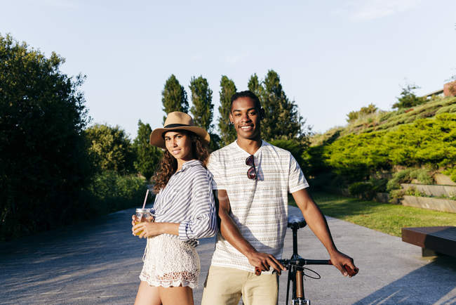 Couple avec boissons et vélo posant au parc urbain — Photo de stock
