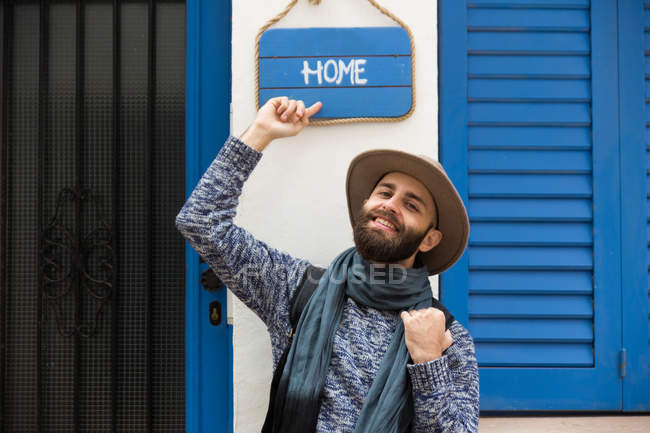 Homme élégant souriant pointant sur l'assiette avec inscription à la maison — Photo de stock