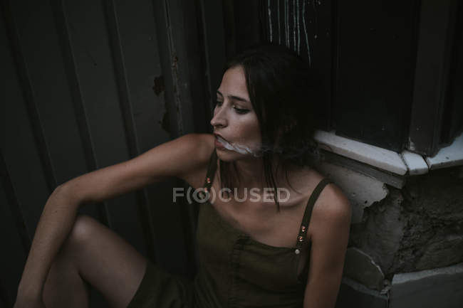 Retrato de mujer morena exhalando humo de cigarrillo y mirando hacia otro lado pensativamente - foto de stock