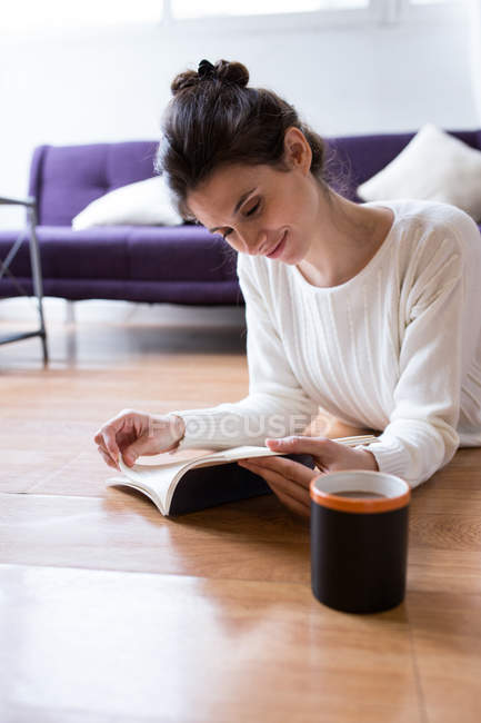 Портрет брюнетки, лежащей на полу с чашкой кофе и книгой для чтения — стоковое фото