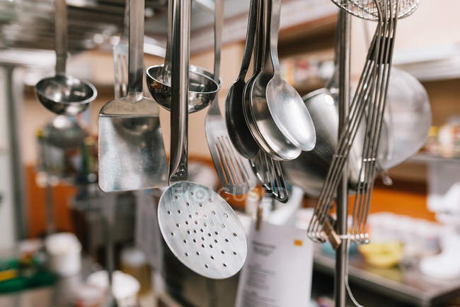Vista de cerca de cucharones y espátulas colgando en la cocina del restaurante - foto de stock