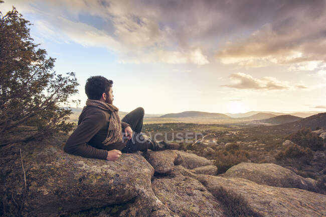 Чоловік лежить на скелях розмірковує про захід сонця над селом — стокове фото