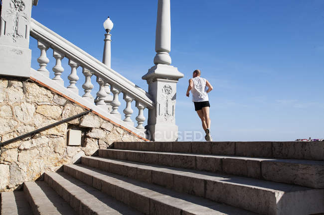 BARCELONA, SPAIN - 17 June, 2011: Back view of man in sportive clothing running up stairs on background of blue sky. — Stock Photo