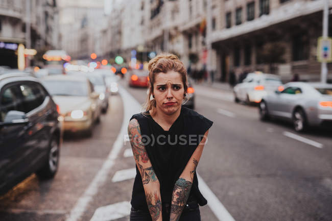 Porträt eines lustigen blonden Mädchens mit tätowierten Armen, das verwirrt auf der Straße wegschaut. — Stockfoto
